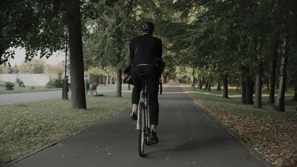 Young Man Riding a Bike in City Park Wearing Business Suit and Helmet Back View