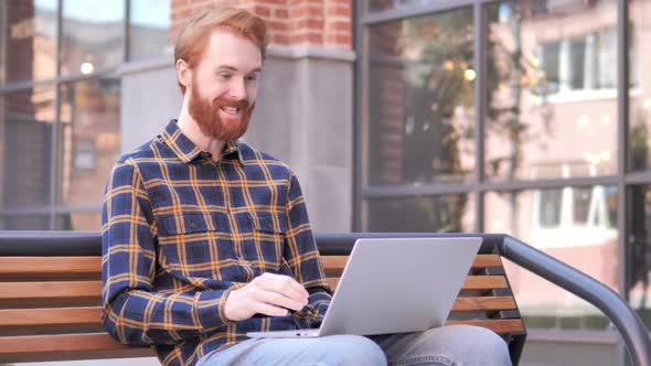 Online Video Chat on Laptop By Redhead Beard Young Man Sitting on Bench