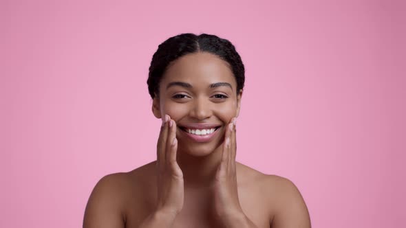 Young Beautiful Black Woman Rubbing Moisturizing Cream Dots on Her Cheeks Smiling to Camera with