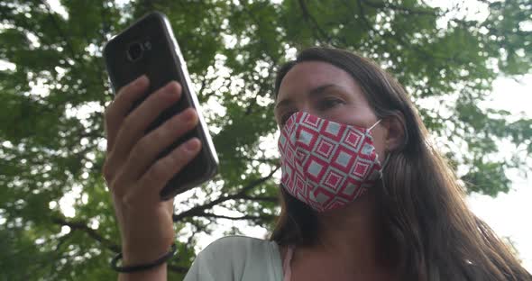 Young Woman with Mask in Park Using Cellphone