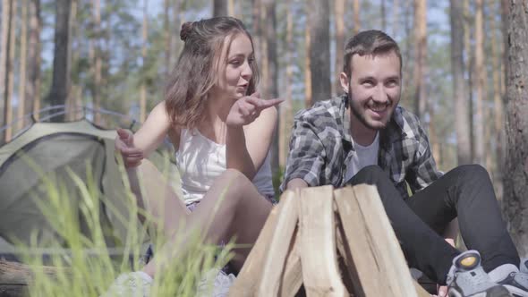 Portrait Handsome Young Man Kindling a Fire in the Forest While Beautiful Young Woman Sitting Near