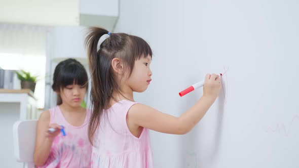 Asian young sibling kid girl enjoy paint on white wall in living room.