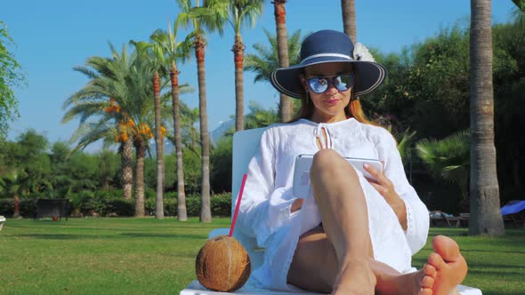 Young Woman Writes and Draws on a Tablet While Sitting on a Deck Chair