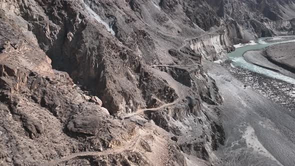 Aerial View Of Winding Old Silk Road Through Rugged Arid Mountains Beside River