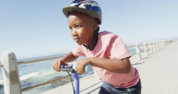 Video of happy african american boy riding scooter by sea