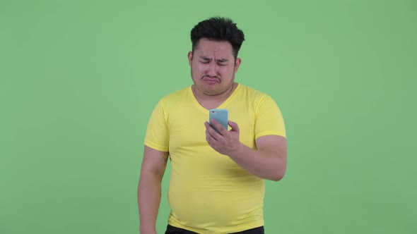 Stressed Young Overweight Asian Man Using Phone and Getting Bad News