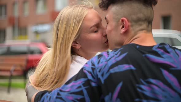 A young couple sits on a bench in the city and communicates, kisses