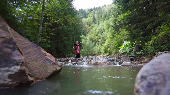 Female cellist among mountain river. Woman playing the cello