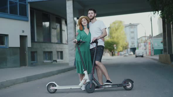 Portrait of Happy Couple in Love Stands in Embraces with Electric Scooters