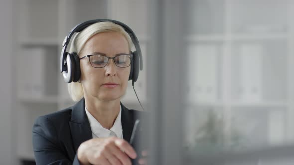 Mid-Aged Businesswoman Using Smartphone and Enjoying Music at Work