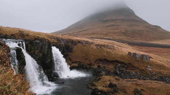 Slow tracking shot of Kirkjufellsfoss Waterfall and Kirkjufell, Iceland in cold mist.