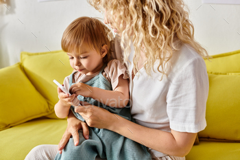 Modern parenthood: curly haired mother engages toddler with cell phone