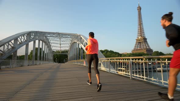 A couple running across a bridge with the Eiffel Tower