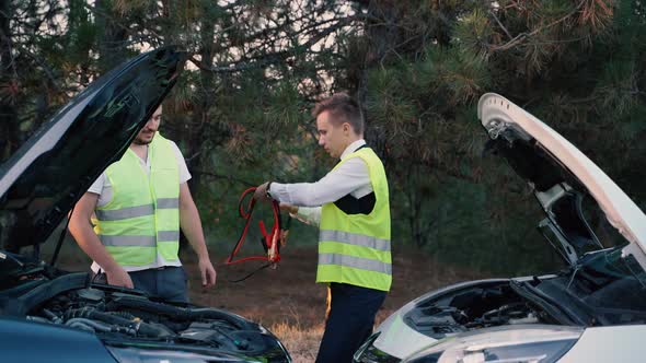 Two Men in a Green Safety Vest are Talking to Each Other Recharging Battery on the Road