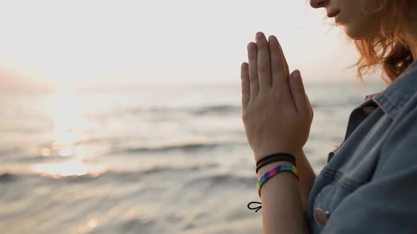 LGBT Pride: Hands Close View of Young Woman Wearing Rainbow Bracelet and Praying at Sea