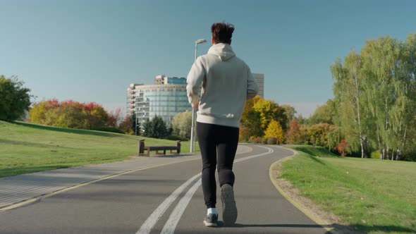 Man Running on Jogging Track at the City Park in Sunny Autumn Morning Back View