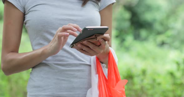 Housewife using cellphone and holding plastic bags in the park