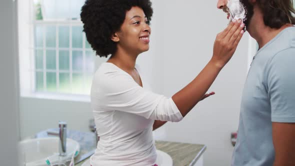 African american woman applying shaving cream on the face of her husband at home