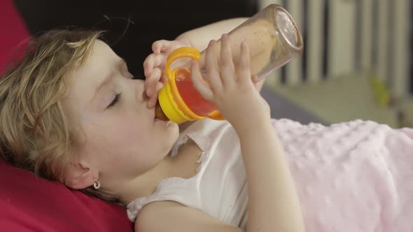 Cute Baby Girl Sleeping on Cozy Bed at Home and Drinking Juice From Bottle