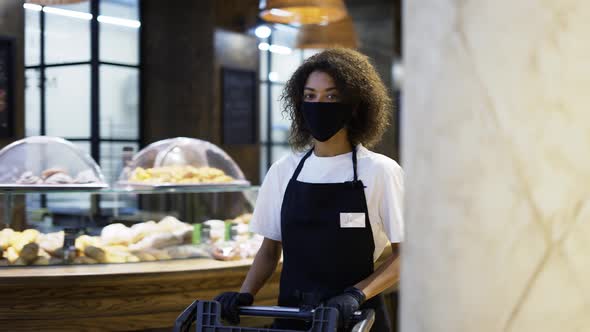 African American Female Worker Pushing Trolley in Supermarket Wearing Protection Mask