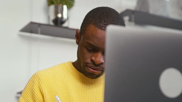 African man student taking notes in notebook using laptop