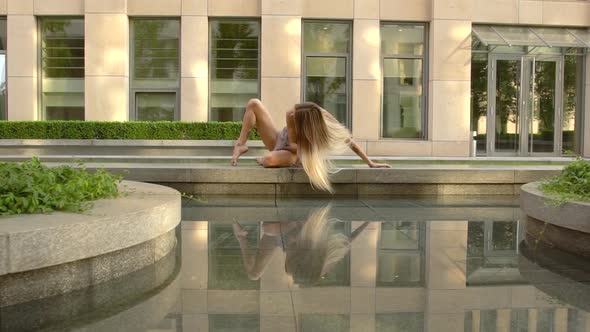 Beautiful Young Girl Dancing on the Street of a Modern City and Is Reflected in the Water. Slow