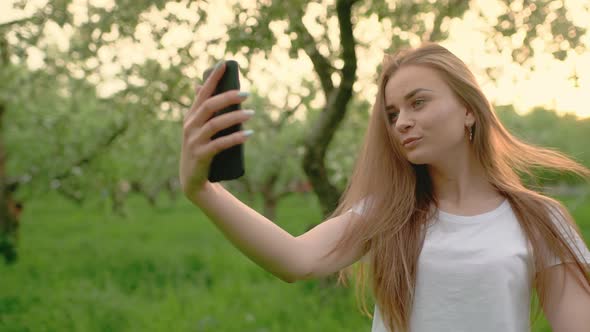 Attractive Blonde Girl Smiling While Taking a Selfie Using a Smartphone