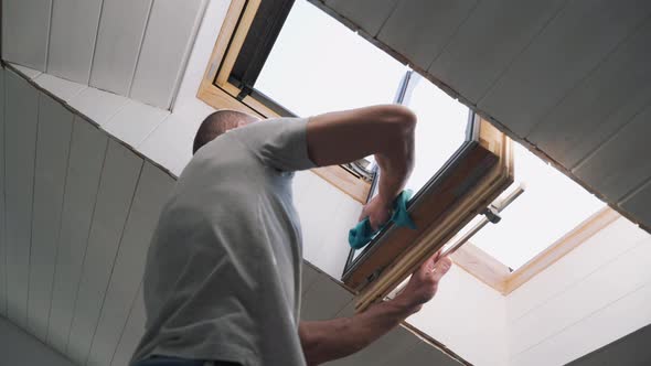 Caucasian Man Washes the Attic Window Bright Sun Illuminates the Man in the Window During the Repair