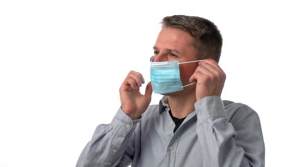 A Young Man on a White Isolated Background Puts on a Surgical Mask To Protect From Allergens and