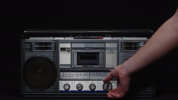 A Man's Hand Turns the Frequency Adjustment Knob of an Old Fm Receiver on a Black Background