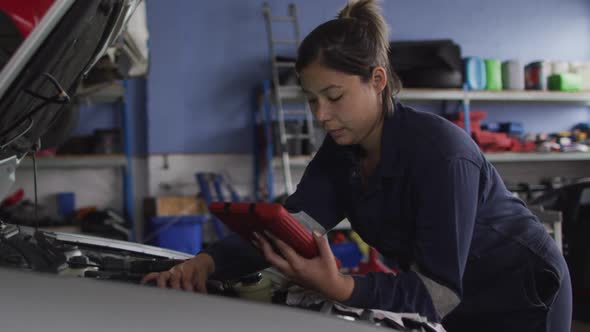 Female mechanic using digital tablet and inspecting the car at a car service station