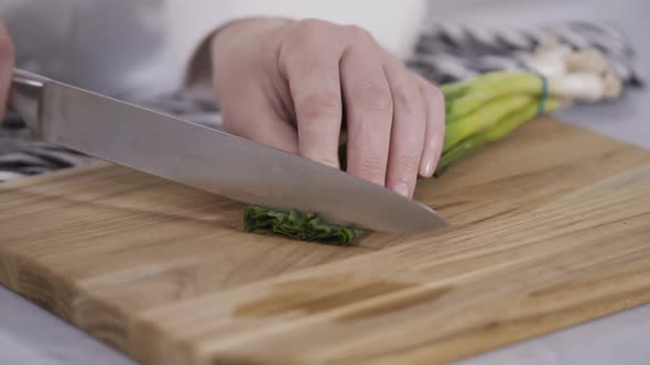 Step by step. Chopping organic green onions on a wood cutting board.