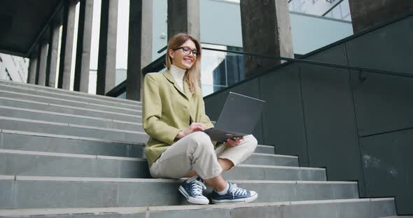 Smiling Woman with Laptop Having Online Video Chat While Sitting on the Stairs.