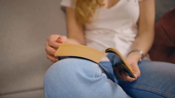 Close View Woman Reads Book and Turns Page Sitting on Sofa