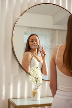 Middle aged female using anti-aging electric massager does led therapy facial massage...