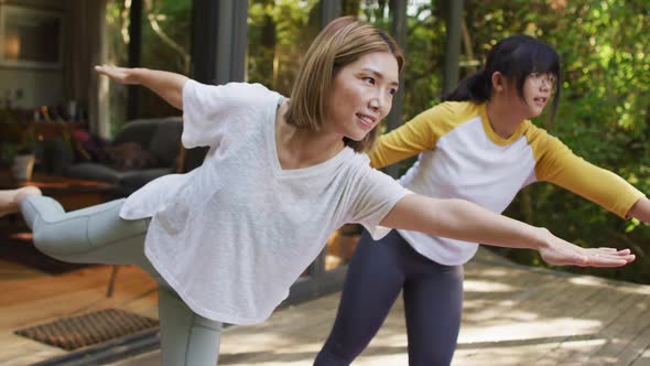 Asian mother and daughter practicing yoga outdoors in garden