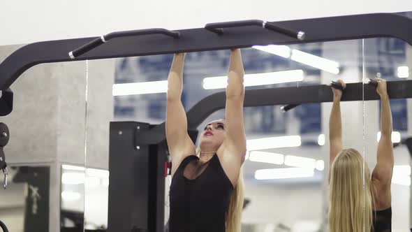 Athletic Young Blond Female Training on Horizontal Bar in Black Sportswear in Gym Performing Pullsup