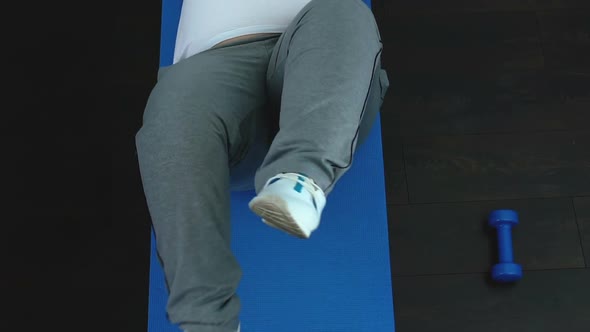 Lazy Chubby Male Doing Bicycle Exercise Lying on Sport Mat During Fitness Lesson