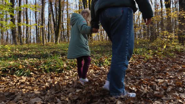 In slow motion, mother and daughter holding hands are walking through an autumn forest