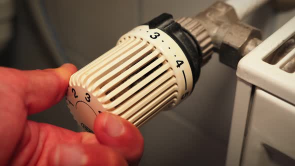 Hand adjusting temperature on heating radiator thermostat