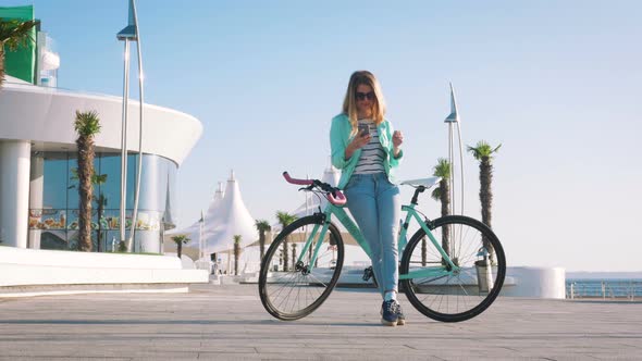 Attractive Female Using Smart Phone While Relaxing in the Fresh Air at Seafront with Her Bike