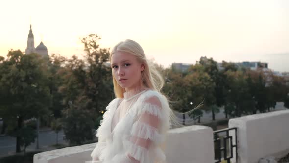 Cinematic Side View of a Wonderful Young European Blonde in a Stylish White Dress Effectively