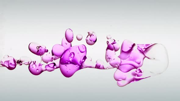 Oddly Satisfying slow-motion floating vivid purple oil against off white background in clear water.