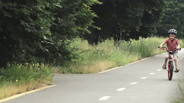 Child riding bicycle on the bike path at rain. Kid in helmet learning to ride at summer