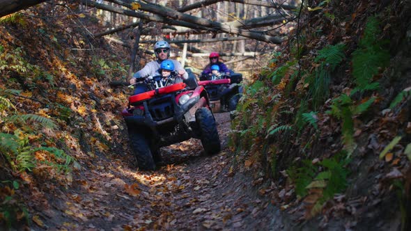 People Rides ATVs in the Woods on the Narrow Path with Trees Above the Path - Autumn Time