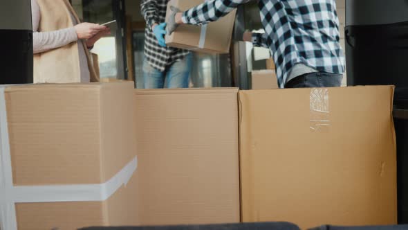 Cardboard Boxes Are Loaded Into the Trunk of the Van. The Man with the Tablet Keeps the Calculations