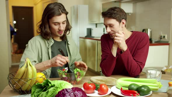 An Attractive Man is Mixing the Salad and Talking with His Friend