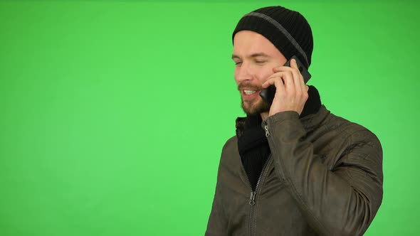 A Young Man in a Winter Outfit Talks on a Smartphone, Then Smiles at the Camera - Green Screen