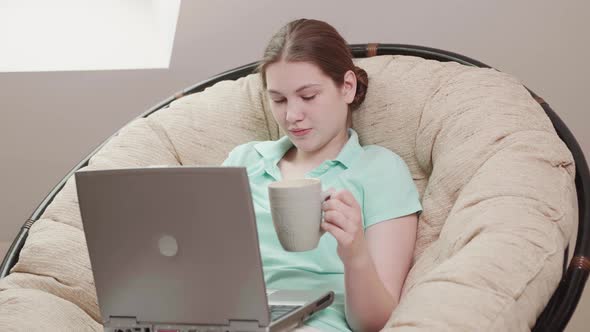 Young girl works remotely from home on bed at the computer.