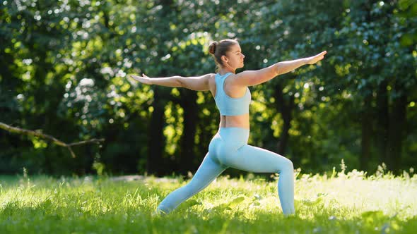 Young woman sportive trainer changes yoga positions stretching on green meadow